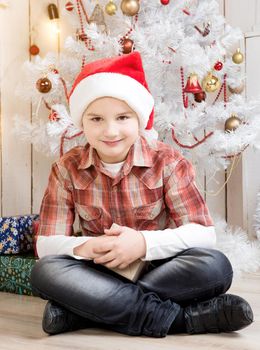 little boy in red hat taking present box near new year tree in decorated room