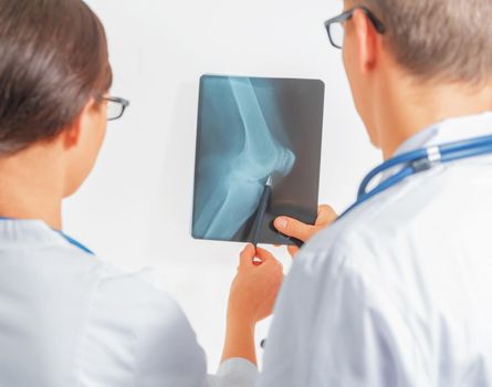 Two doctors look at x-ray picture of the knee joint, rear view