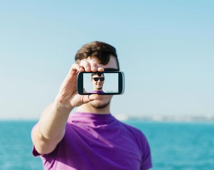 Young handsome man doing a self-portrait with smartphone on background of sea