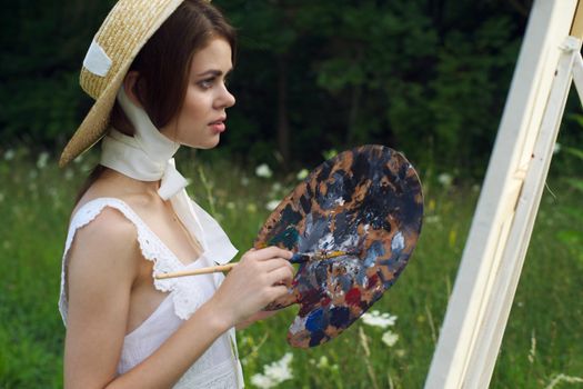 woman with a palette of paints painting a picture outdoors close-up. High quality photo