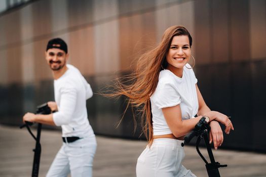 A girl and a guy are walking on electric scooters around the city, a couple in love on scooters