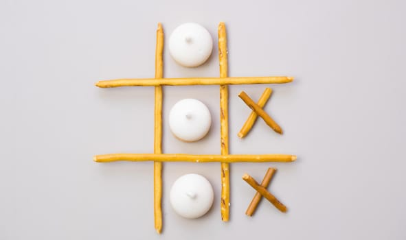 Creative mockup of tic-tac-toe game made from crackers and cookies sticks on gray background. Food concept. Edible snacks dry sticks with salt and cookies on a white plate. Straws, crackers sticks