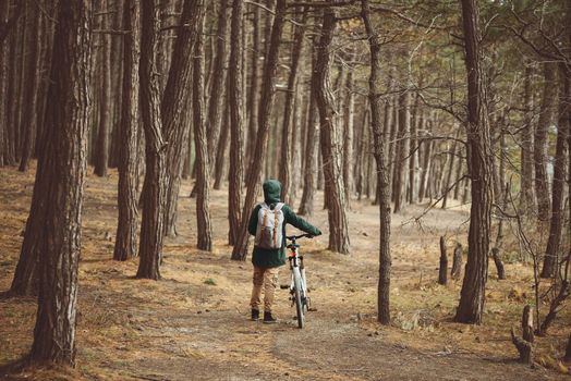 Hiker woman with backpack walking with bicycle in pine forest