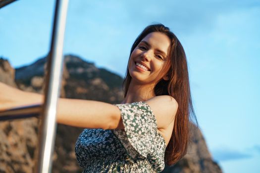 Young pretty woman in floral dress posing on yacht in the sea