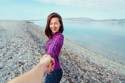 Couple in love. Smiling beautiful young woman holding man's hand and leading him on beach near the sea