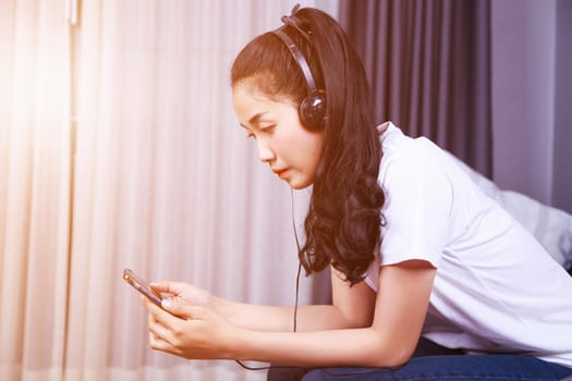 young woman listening to music in headphones with moblie on sofa at home