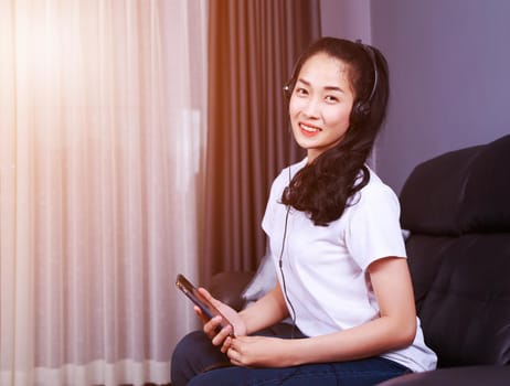 young woman listening to music in headphones with moblie on sofa at home