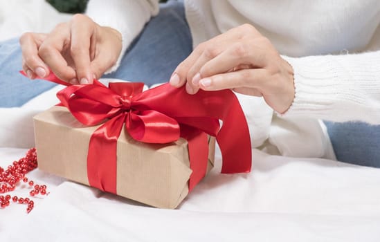 Happy Holidays. Female hands untie a bow on a gift box for Christmas in a white bed