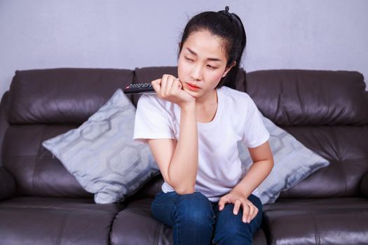 woman with tv remote control on sofa in living room at home