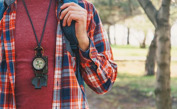 Traveler young man with backpack and compass walking in summer forest