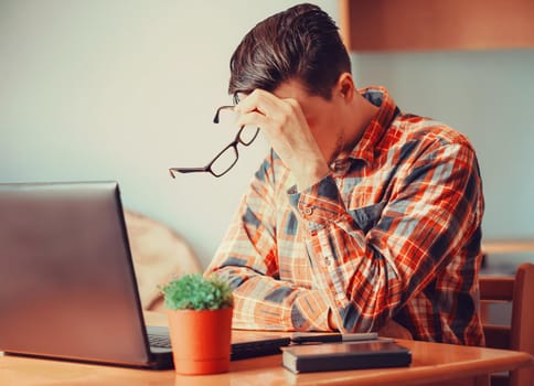 Tired young man sitting over laptop in the office