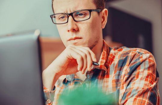 Pensive young man working over laptop in the office