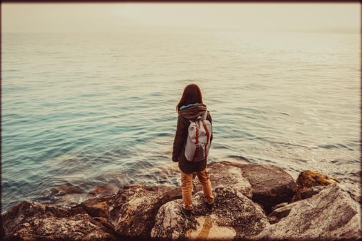 Traveler young woman standing on stone coast and enjoying view of sea. Image with vintage color effect and rectangular frame