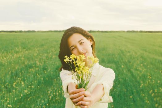 Beautiful young woman with a bouquet of yellow flowers on summer meadow. Focus on face