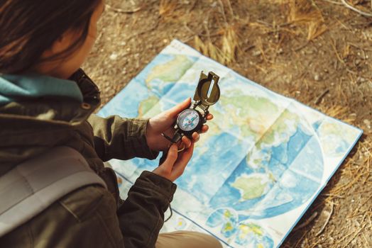 Traveler young woman searching direction with a compass on background of map in the forest