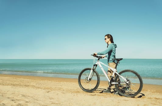Beautiful young woman walking with a bicycle on beach in summer