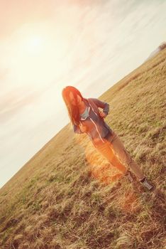 Beautiful young woman with backpack walking on summer meadow. Image with sunlight effect