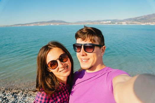 Happy young loving couple taking self-portrait on beach on background of blue sea in summer