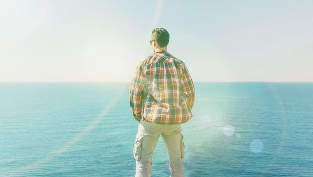 Young man enjoying view of sea in summer, rear view. Image with sunlight effect