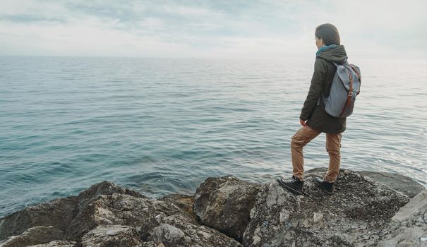 Traveler young woman standing on stone on coast and enjoying view of sea