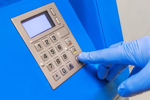 A man's hand in protective medical gloves dials a pincode at the terminal for issuing money, close-up.