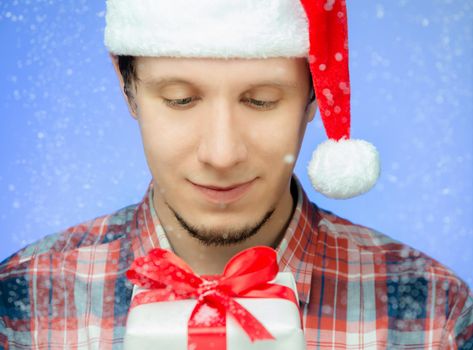 Happy man in santa hat with a gift box in the snow on blue background