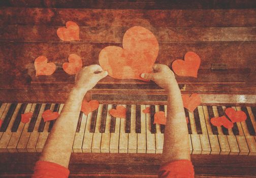Unrecognizable child holds red paper heart on a background of piano, close-up. Vintage image