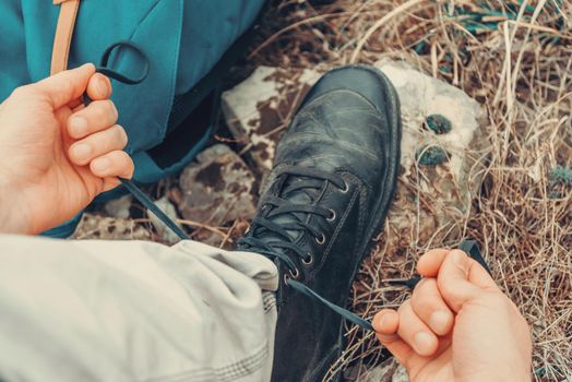 Hiker man tying shoelaces on nature outdoor, near backpack. Point of view shot