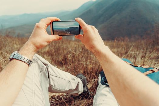 Hiker man taking photographs mountain landscape with smartphone. Point of view shot