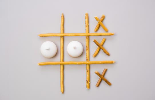 tic-tac-toe from crackers and sticks on a beige background. Food concept. Edible snacks dry sticks with salt and cookies on a white plate. Straws, sticks for crackers