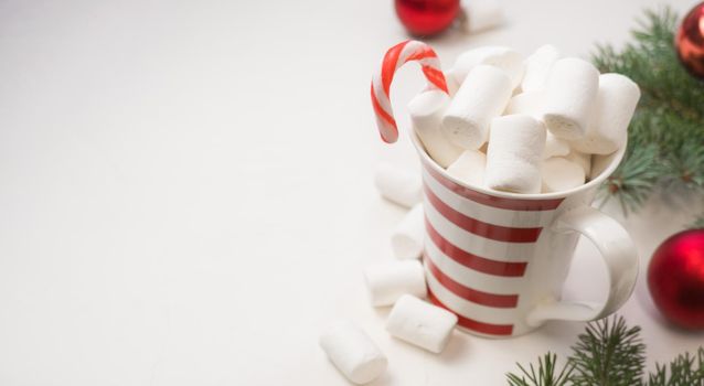 hot chocolate with marshmallows in a red and white bakery on a white background and branches of a New Year tree