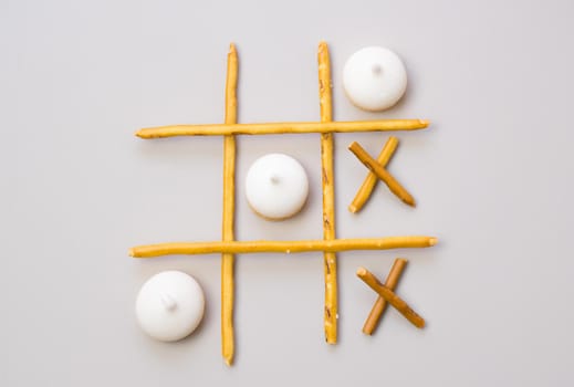 tic-tac-toe from crackers and sticks on a gray background. Food concept. Edible snacks dry sticks with salt and cookies on a white plate. Straws, sticks for crackers