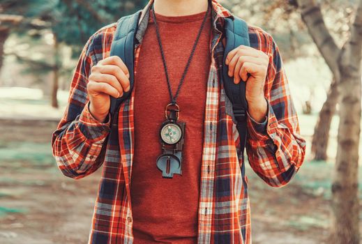 Tourist young man with backpack and compass walking in summer forest