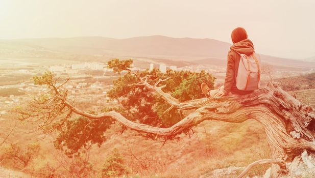 Traveler young woman sitting on a tree in the mountains. Image with sunlight effect