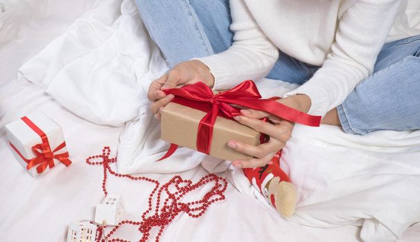 Woman wraps ecological Christmas gifts in wrapping paper, satin ribbon, sitting in a white bed with Christmas decorations.