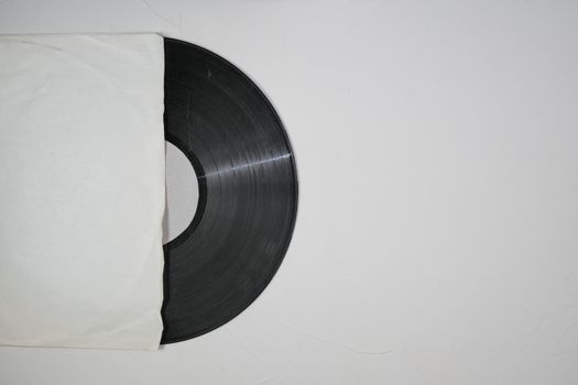 Old vinyl record in paper case on white marble background.