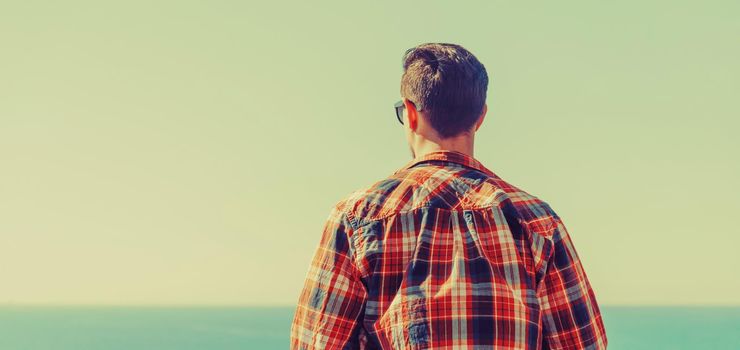 Young man enjoying view of sea, rear view. Image with instagram filter