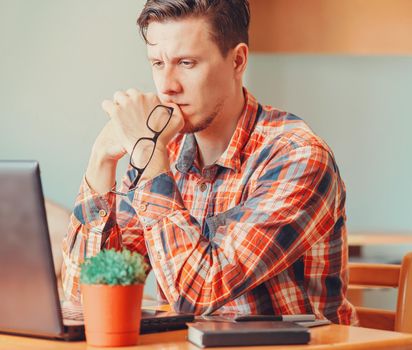 Pensive young man looking on laptop in the office