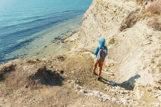 Traveler girl with backpack walking on coastline near the sea in summer