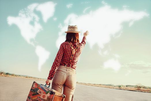Traveler woman with vintage suitcase waves her hand to map of the world. Concept of travel