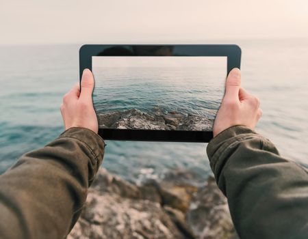 Woman taking photographs coast on tablet PC. Point of view shot