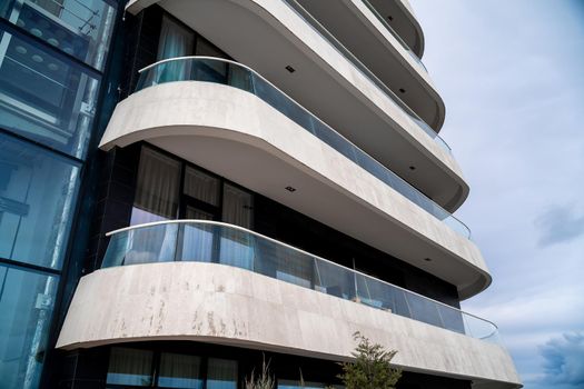 A corner of a modern building with a row of white balconies against the sky. On the left you can see the elevator