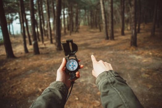 Traveler woman holding a compass and pointing direction in the forest. Close-up. Point of view shot
