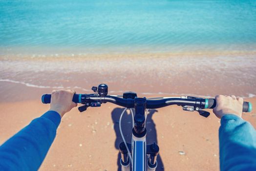 Woman holding handlebar of bicycle on beach in summer. Point of view shot