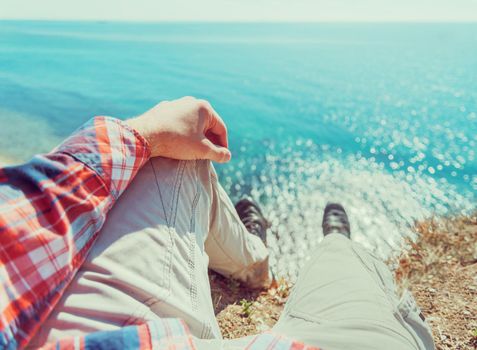 Man sitting on coast near the sea. View of legs. Point of view shot