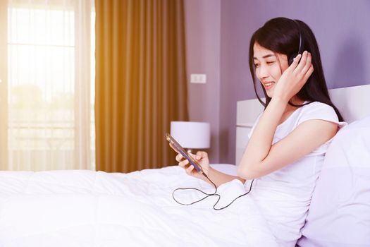 woman in headphones listening to music from smartphone on bed in the bedroom