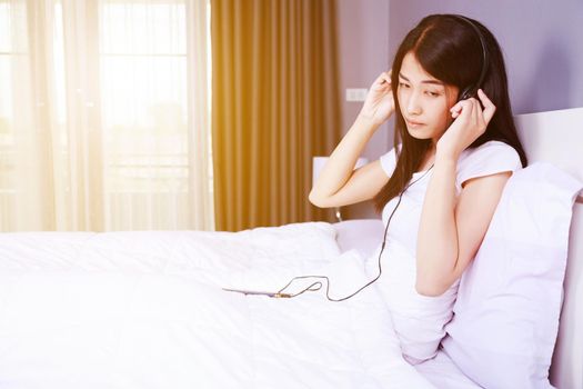 woman in headphones listening to music from smartphone on bed in the bedroom