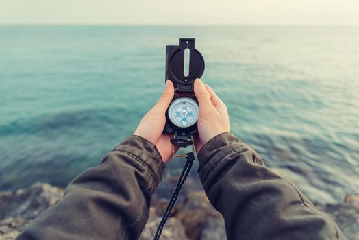 Traveler woman searching direction with a compass on stone coastline near the sea. Point of view shot. Image with instagram filter