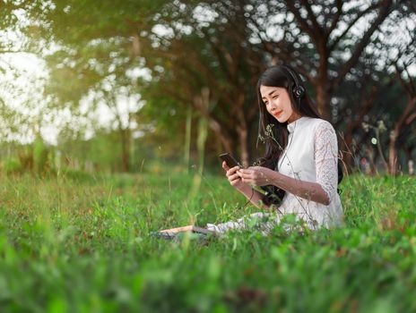 woman with headphones listening to music from smart phone and sitting in the park