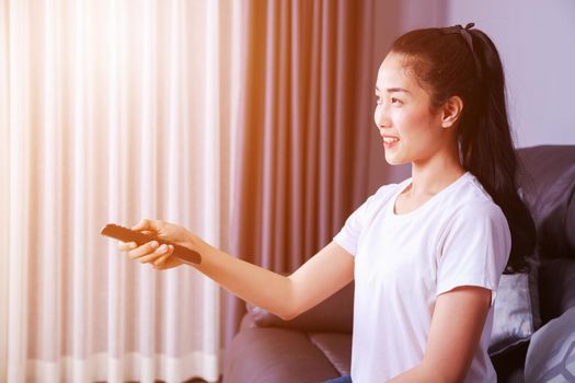 woman with tv remote control on sofa in living room at home